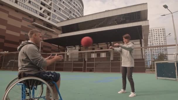 人们在篮球场上练习 跟踪坐在轮椅上的白种人和相互投掷球并投入篮筐的年轻女子 — 图库视频影像
