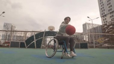 Düşük açılı, tekerlekli sandalyedeki beyaz kadın basketbol sahasında salya akıtıyor.