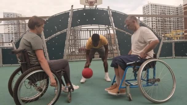 若いアフリカ系アメリカ人バスケットボールコーチの訓練の広いショット屋外コートで車椅子で白人女性と男性選手 — ストック動画