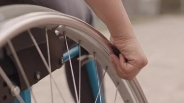 Tekerlekli sandalyesinin dönen çarkını çeviren, dışarıda yürüyen, tanınmayan bir insanın yakın çekimi.