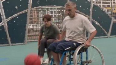 Mahallede basketbol oynayan, tekerlekli sandalyeli mutlu beyaz kadın ve erkek amatörlerin el bilgisayarı.