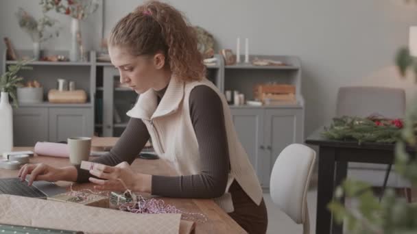 Keskipitkä Nuori Kiharatukkainen Valkoihoinen Nainen Istuu Kirjoituspöydän Ääressä Käsityöliikkeessään Katselee — kuvapankkivideo
