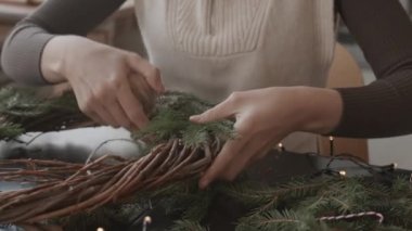 Gündüzleri atölyesinde masa başında oturan, Noel çelengi yapan, makasla sicim kesen kırpık kadın.