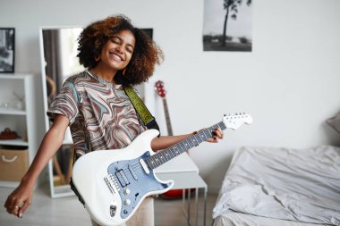 Gülümseyen genç kız gitar çalıyor.