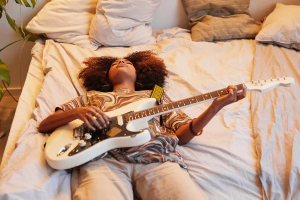 Jonge vrouw speelt gitaar op bed — Stockfoto