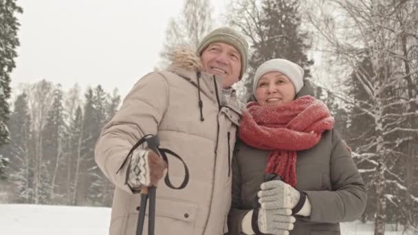 低い角度中のシニア白人男性抱擁し 彼の幸せなアジアの妻と話して 雪の冬の日に公園に立っているカップル — ストック動画