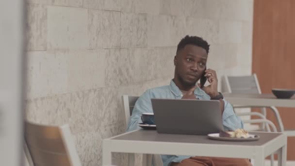 中等身材的黑人年轻人 坐在户外餐桌旁 早餐时使用手提电脑 用手机交谈 喝咖啡 — 图库视频影像