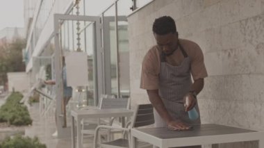 Orta uzunlukta önlük takan, masaya temizleyici sıkan ve arka plan üzerinde çalışan, bulanık iş arkadaşı.