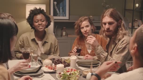 6人の若い多民族の友人の中程度のクローズアップ自宅で夕食のテーブルに座って 話をし 笑って その後 ワイングラスを上げ クリンクして笑顔 — ストック動画
