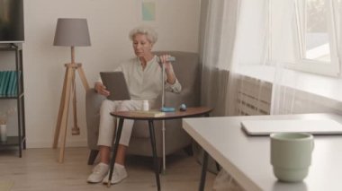 Kafkasyalı son sınıf öğrencisinin bastonuyla koltukta oturup dijital tablette görüntülü konuşma yaparken çekilmiş bir fotoğrafı.