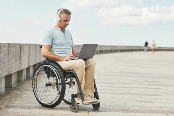 Hombre adulto en silla de ruedas con ordenador portátil al aire libre —  Fotos de Stock