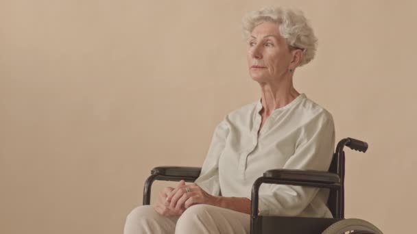 坐在轮椅上的白人老年妇女的中等肖像 在孤立的米色背景下摆出拍照姿势 — 图库视频影像