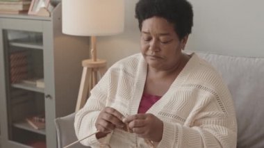 Yaşlı Afrikalı Amerikalı kadının gündüz vakti evinin kanepesinde oturup örgü ördüğü orta boy yakın plan çekimleri, tatlı küçük torunu ona doğru koşuyor ve büyükannesine sarılıyor.