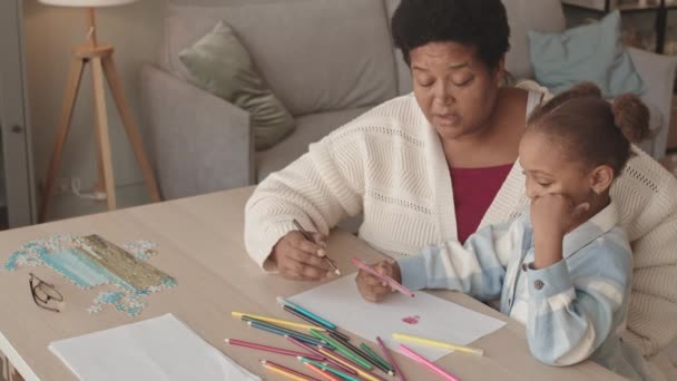 一个快乐的五岁小女孩白天坐在客厅的办公桌前 手握毛笔和铅笔 坐在非洲裔美国人祖母的膝上 一边聊天一边画画 — 图库视频影像