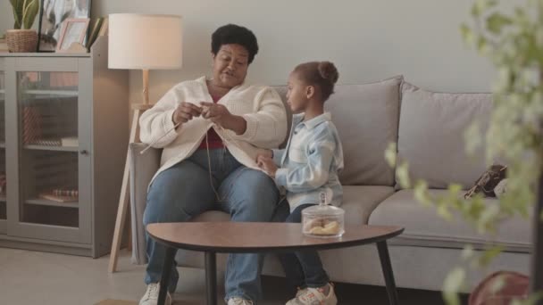 全镜头是成熟的非洲裔美国妇女编织和她可爱的小孙女 白天坐在家里沙发上 微笑着聊天 — 图库视频影像