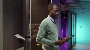 Elinde dijital tabletle sunucu odasından çıkıp kameraya bakan Afrikalı genç bir IT yöneticisiyle orta boy fotoğraf.