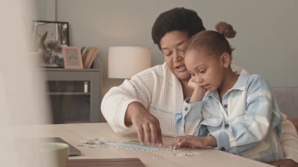 一个中等可爱的5岁小女孩 白天坐在客厅的办公桌前 与她的美籍黑人祖母擦肩而过 一边聊天一边拼图 — 图库视频影像
