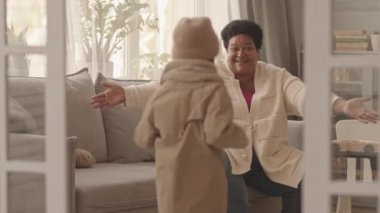 Orta yaşlı Afrikalı Amerikalı bir kadının gün içinde oturma odasında kanepede oturup, örgü şapka ve eşarp takıp eve gelirken küçük sevimli torunuyla tanışması ve kucaklaşması.