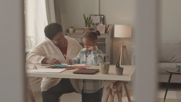 一个中等身材的小女孩 白天身穿两条马尾辫 站在房间里可爱的非洲裔美国人祖母身旁 一边笑一边用毛笔和铅笔在桌上画画 — 图库视频影像