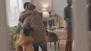 Farklı nesillerden kadın ve erkek Siyahi aile üyeleri gündüz yemeğinden önce yemek salonunda selamlaşıyor, sarılıyor ve tokalaşıyor.