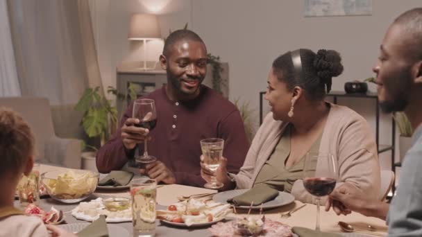 在家中度假时 快乐的黑人男女家庭成员坐在餐桌旁 进行交谈 然后举杯 进行中等程度的亲密接触 — 图库视频影像