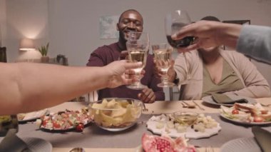 Evde yemek masasında oturan mutlu siyah kadın, erkek ve tanınmayan aile üyeleriyle kadehleri tokuşturan yavaş hareket eden kişi.