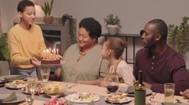 On yaşındaki siyahi bir kızın doğum günü pastasını mutlu büyükannenin önüne koyması ve mumları üflemesi, aile arasında kutlama yapması.