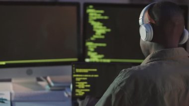Kulaklık takan Afrikalı-Amerikalı programcının yavaş çekimleri bilgisayara program kodları yazarken kameraya dönüp gülümsüyor ve geceleri yalnız çalışıyor.