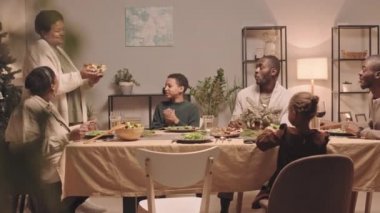 Orta uzunlukta Afrika kökenli Amerikalı bir kadın aile üyelerine kızarmış tavukla servis yapıyor. Evde yemek masasında oturuyor, Noel 'i kutluyor, el çırpıyor ve akıllı telefondan film çekiyor.