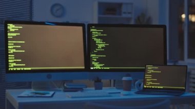 Siyah arka planda program kodları olan ve gece geç saatlere kadar çalışan iki monitör ve dizüstü bilgisayarla masada oturan Afro-Amerikalı programcının dikiz görüntüsü.