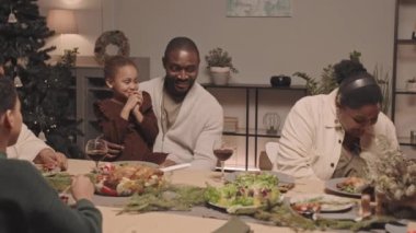 Mutlu siyah kadın, şenlik masasında oturuyor. Genç babasının kucağında Noel hediyesiyle oturan küçük tatlı kızına sürpriz yapıyor.