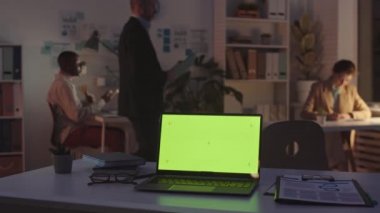 Gece geç saatlere kadar birlikte çalışan üç meslektaşın çalıştığı karanlık ofisteki masada mali belgelerle birlikte bilgisayarın yavaş çekimleri.