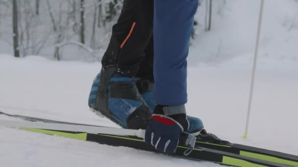 高个子白人男子在森林里的白雪上把靴子系在越野滑雪板上 然后滑走了 — 图库视频影像