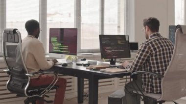 Çağdaş ofis bilgisayarlarında program kodları yazan iki erkek yazılım geliştiricisinin ya da mühendislerin dikiz görüntüsü