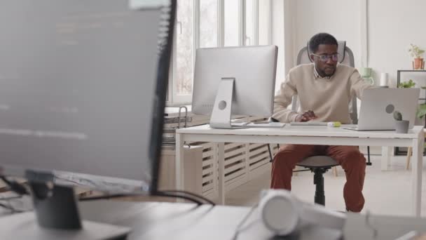 現代のオフィスの机に座ってコンピュータに取り組んで若いアフリカ系アメリカ人男性ソフトウェア開発者のスタブショット — ストック動画