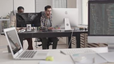 Modern ofisteki bilgisayarlar üzerinde çalışırken iki genç çoklu etnik erkek programcının sohbet ederken çekilmiş fotoğrafı.