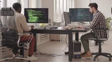 Çağdaş ofisteki ekranlarda program kodları olan bilgisayar üzerinde çalışan iki erkek bilişim uzmanının yavaş çekimleri