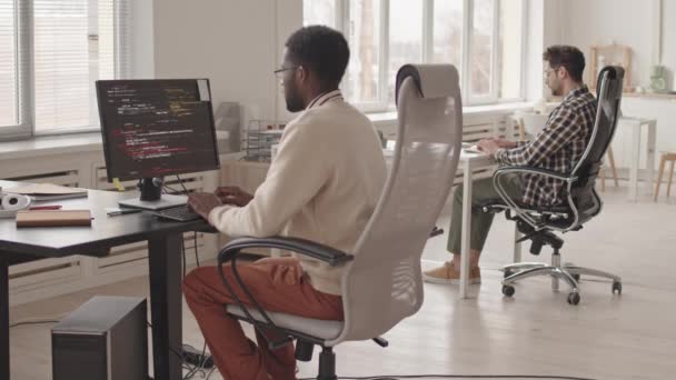現代のオフィスでPc上で働く2人の若い多民族のプログラマーのチームのスタブ スローモショット 黒いモニター画面でプログラムコードを実行する — ストック動画