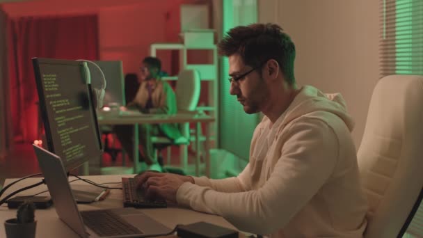 穿着便服和眼镜的大胡子程序员在个人电脑和笔记本电脑上输入程序代码 与办公室同事一起工作 点亮红灯和绿灯 — 图库视频影像