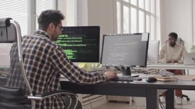 Çağdaş ofiste bilgisayarlar üzerinde çalışan iki genç erkek programcının bıçaklı fotoğrafı. Bilgisayar monitörlerinde program kodları çalıştırılıyor