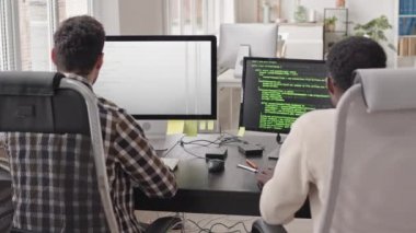 Ofisteki modern bilgisayarlara program kodları yazan iki erkek programcının dikiz görüntüsü.