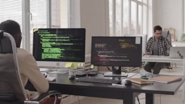 Modern ofis ekranlarında program kodları çalışan bilgisayar monitörleri önünde oturan programcı takımının bıçak görüntüsü.