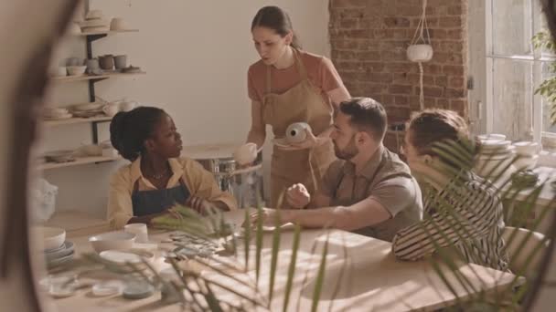中慢镜头下 一小群多民族的人围坐在桌旁的陶器作坊 女性陶工向她们展示粘土制品的例子 — 图库视频影像