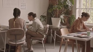 Modern ofiste takım halinde çalışan dört genç yaratıcı tasarımcının planlarını ve planlarını tartışırken çekilen görüntüler.