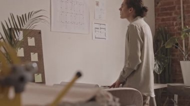 Ofiste birlikte çalışan iki genç erkek iç mimarın bina planları ve planlarını tartışırken orta yavaş çekimi.