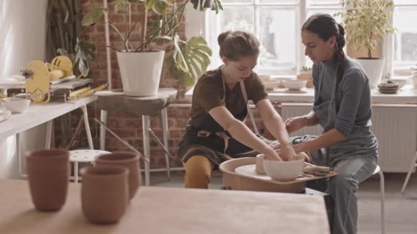 在舒适的车间里 两名年轻女子坐在陶瓷轮旁边 与粘土一起工作 并在交谈 拍了一张慢镜头 — 图库视频影像