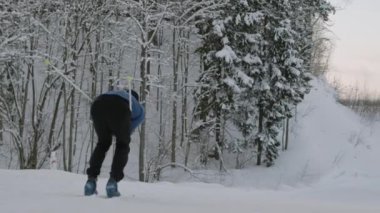Tanınmayan bir sporcunun kıçı kilitlenmiş, spor kıyafetler giymiş, ormandaki beyaz kabarık kar üzerinde kayak yapıyor.