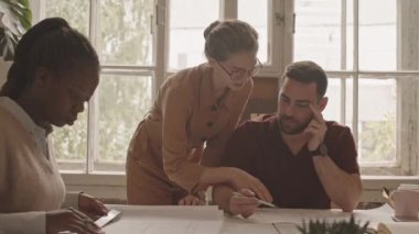 Tasarımcılardan oluşan profesyonel bir ekibin projeyi çizerek, fikirleri tartışarak, modern tasarım ajansında büyük bir masada çalışarak oluşturduğu yavaş çekim.