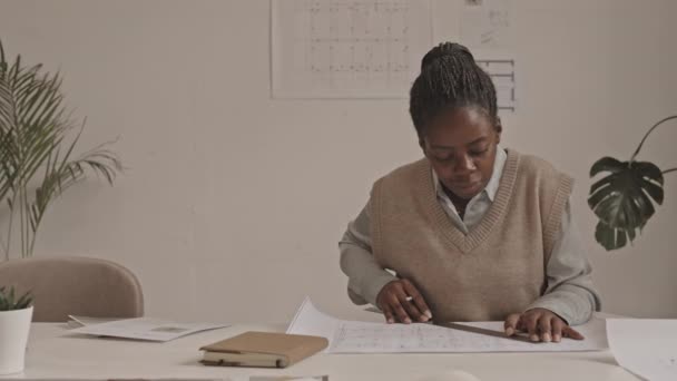 チームとプロジェクトの詳細を議論するテーブルで青写真を描く若いアフリカ系アメリカ人女性建築家の中程度のショット — ストック動画