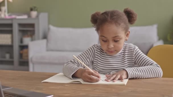 Slowmo Media Close Upの可愛いです5歳のアフリカ系アメリカ人の女の子書き込みでCopybookながら勉強オンライン上のラップトップに座ってデスクで居心地の良いリビングルーム — ストック動画